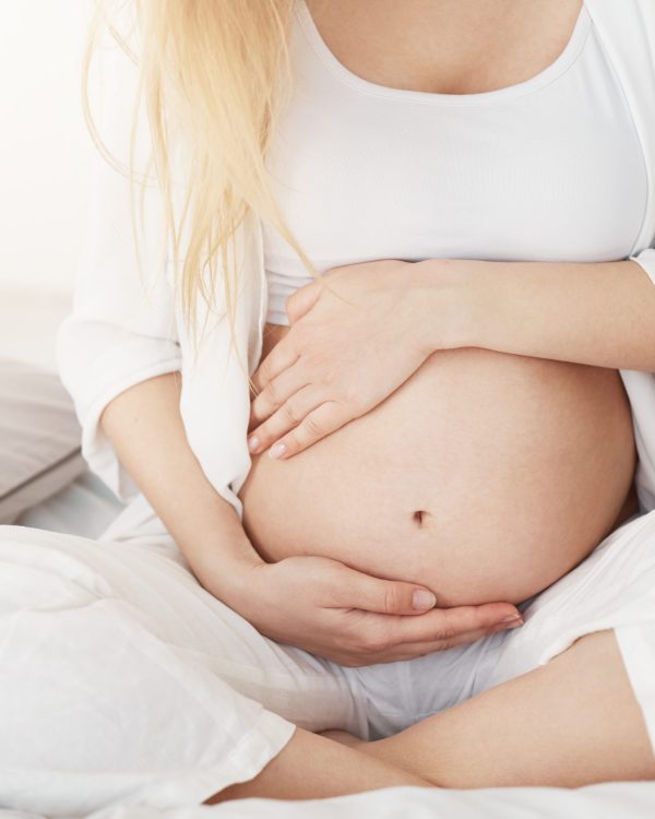 Young pregnant lady touching her belly sitting in her bedroom in afternoon. Pregnancy concept.